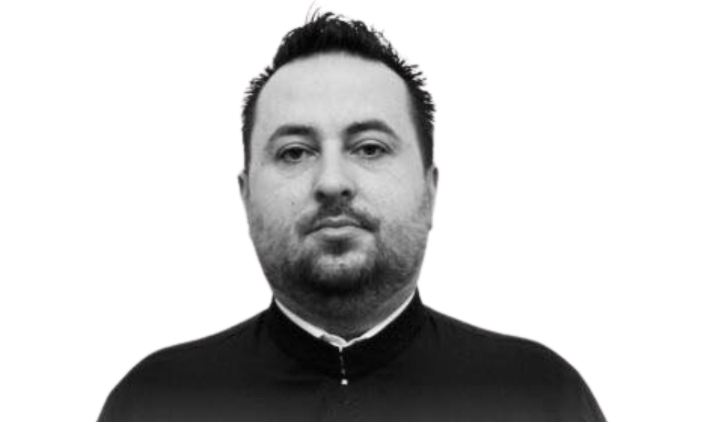 Fotografie a părintelui Ionuț Simion Ciutre, în veșminte preoțești, zâmbind blând în fața bisericii